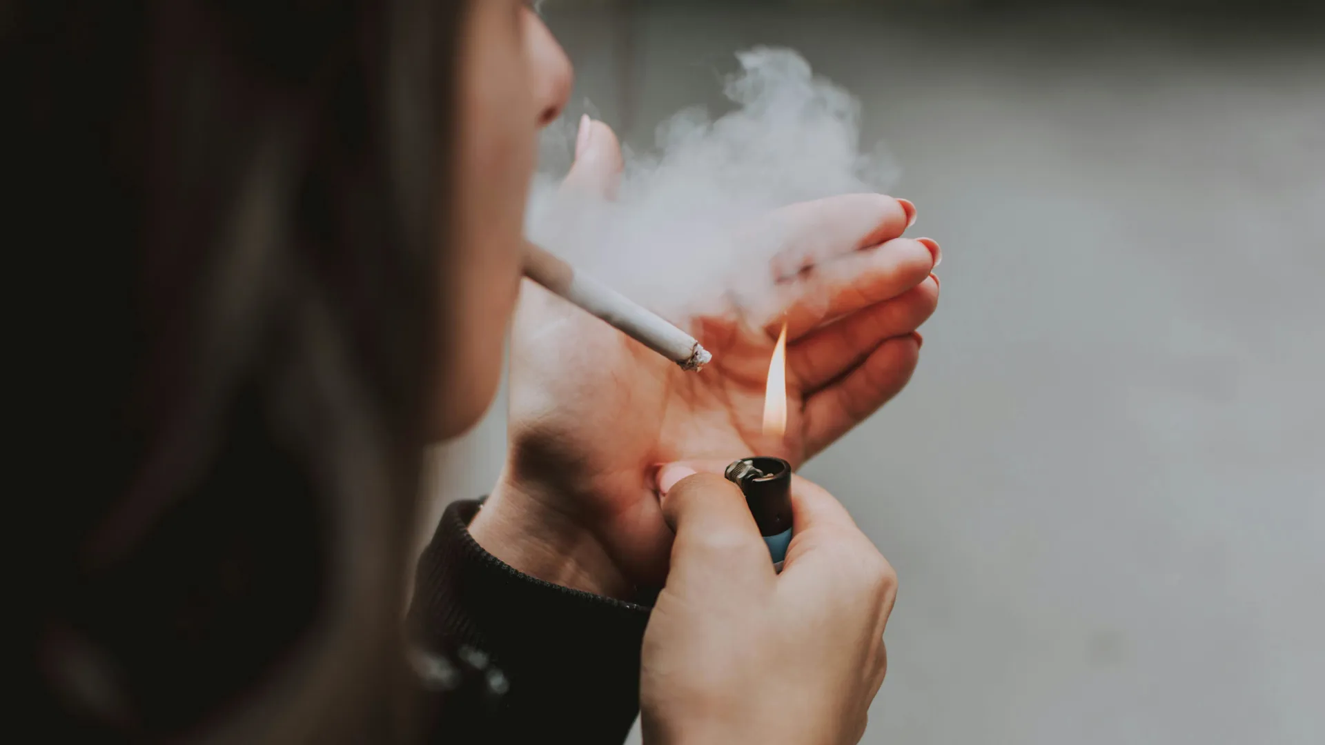 A young woman lights her next cigarette, showing a clear addiction to smoking.