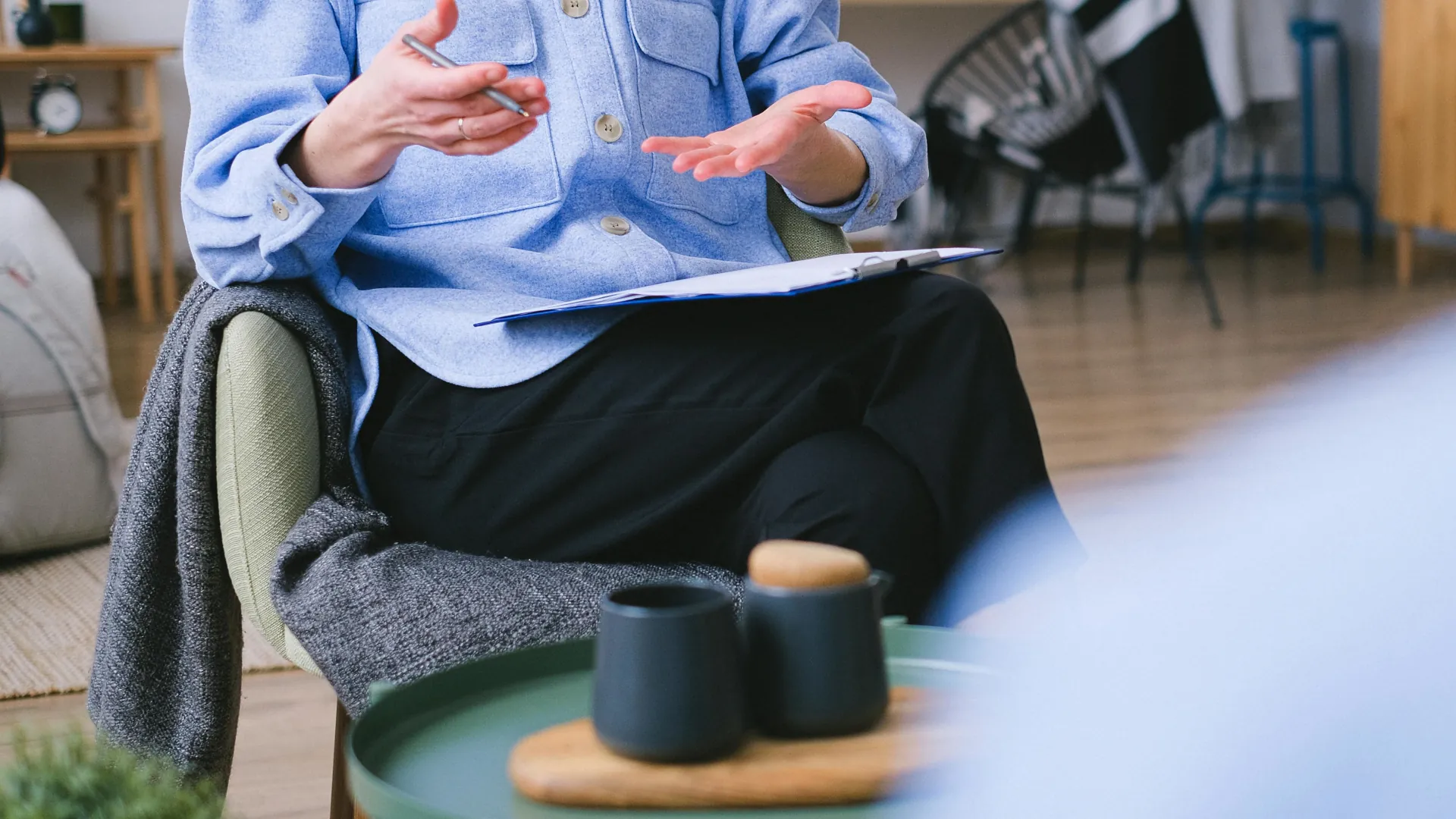 A relationship counsellor is trying to smooth through things with a couple. She can be seen with her hands in gesture trying to answer their calls for help.