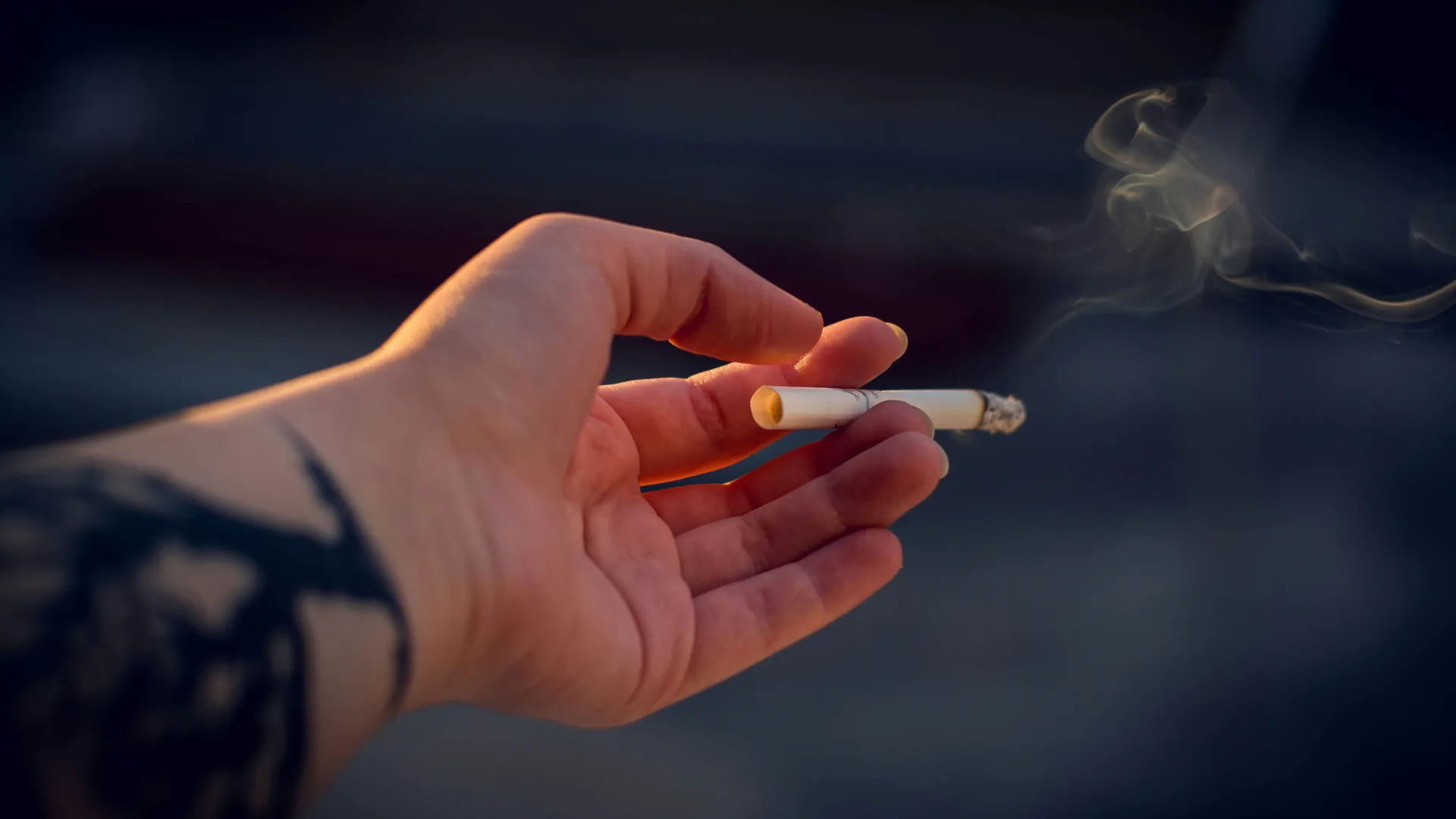 Person with a tattoo holding a lit cigarette.